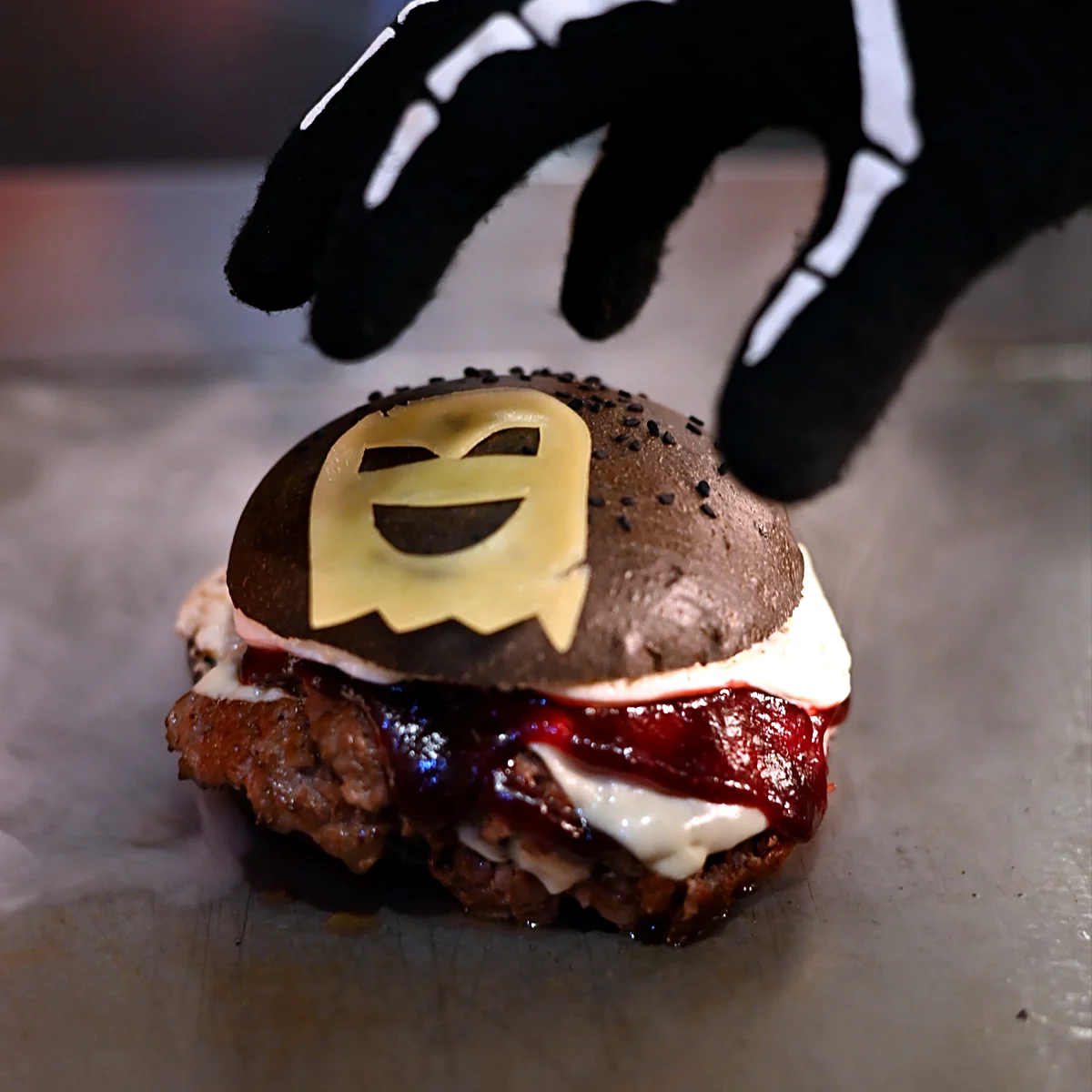 Mano con guante de esqueleto tomando una Boo Burger de pan negro